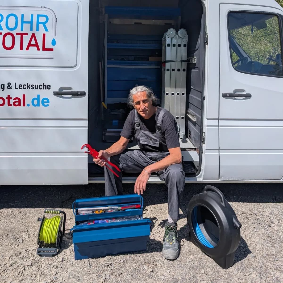 Grisha Stelzmann von RohrTotal mit Rohrzange, Werkzeugkiste und Spirale am Einsatzfahrzeug